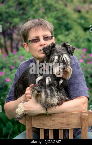 Frau, die mit zwei Miniatur-Schnauzer-Hunden im Freien sitzt. Stockfoto
