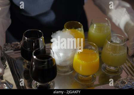 Silbernes Tablett mit einer Vielzahl von kalten Getränken, die von einem Kellner bei einer Veranstaltung getragen werden. Ein Glas mit Trockeneis erzeugt weißen Rauch für das visuelle Interesse. Stockfoto