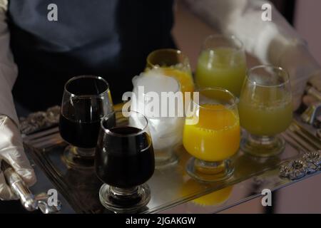 Nahaufnahme eines silbernen, glänzenden Tabletts mit verschiedenen kalten Getränken, die auf einer Party serviert werden. Ein Glas mit Trockeneis erzeugt weißen Rauch für das visuelle Interesse. Stockfoto