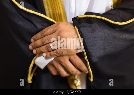 Nahaufnahme der Hände eines Bräutigams mit silbernem Verlobungsring. Die linke Hand des Mannes hält sich an den Ärmel von Bisht, der über Kandora getragen wird, beides traditionelle arabische Kleidung. Stockfoto