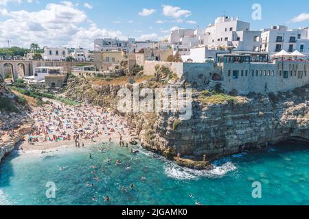 Schöne Luftaufnahme von Polignano a Mare mit weißen Steinhäusern, Klippen, Strand, blaues Meer und Touristen, Badegäste, umgeben von mediterraner Natur Stockfoto