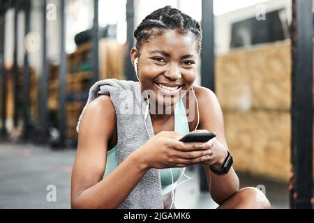 Detaillierte Angaben zu meinem Training in meiner Calorie Tracking App. Eine attraktive junge Frau, die allein im Fitnessstudio sitzt und nach dem Training ihr Handy benutzt. Stockfoto