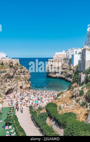 Schöne Luftaufnahme von Polignano a Mare mit weißen Steinhäusern, Klippen, Strand, blaues Meer und Touristen, Badegäste, umgeben von mediterraner Natur Stockfoto
