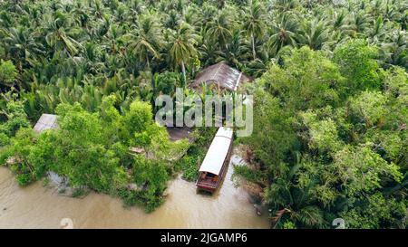 Luftaufnahme von oben nach unten des Bootes, das am Pier entlang der braunen küste des mekong-Deltas im Dschungel von Ben Tre Vietnam angedockt ist Stockfoto