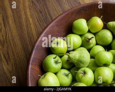 Eine Holzschale, gefüllt mit leuchtend grünen Äpfeln und Birnen Stockfoto