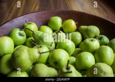 Eine Holzschale, gefüllt mit leuchtend grünen Äpfeln und Birnen Stockfoto