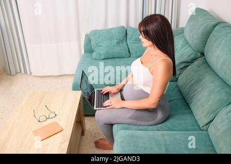 Schwanger junge Frau, die zu Hause mit ihrem Laptop auf dem Sofa arbeitet. Stockfoto