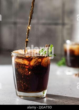 Cola oder cuba Libre Cocktail in Glas mit Eiswürfeln und Minze gießen. Softdrink mit Spritzwasser. Vertikale Ausrichtung Stockfoto
