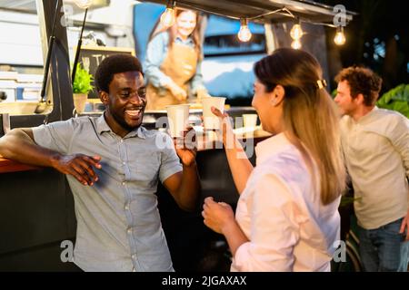 Glückliche multirassische Freunde, die Spaß haben, Bier in einem Straßennahrungs-LKW-Markt zu trinken Stockfoto