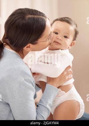 Eine ganze Menge Küsse machen ein glückliches Baby. Porträt eines entzückenden Mädchens, das von ihrer Mutter zu Hause gehalten und geküsst wird. Stockfoto