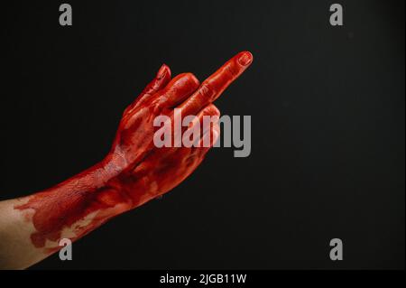Mit Blut befleckte weibliche Hand zeigt den Mittelfinger auf schwarzem Hintergrund. Stockfoto