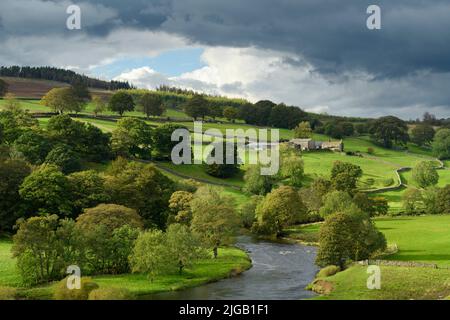 Landschaftlich reizvolle Landschaft im ländlichen Yorkshire Dales Valley (Fluss Wharfe, traditionelles Bauernhaus, Hügel, Bäume am Flussufer, Steinmauern) - Wharfedale, England, Großbritannien.