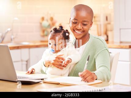 Eine junge Frau, die ihr Baby hält, während sie von zu Hause aus arbeitet. Stockfoto