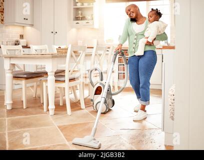 Eine alleinstehende Mutter kann alles. In voller Länge eine attraktive junge Frau, die beim Tragen ihrer Tochter zu Hause saugt und einen Telefonanruf abgibt. Stockfoto