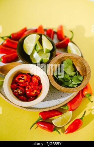 In Scheiben geschnittene rote, würzige Chilischoten, Koriander und Limette auf einem Teller als Beilage für eine Thai-Suppe Stockfoto