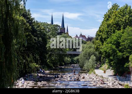 09. Juli 2022, Baden-Württemberg, Freiburg: Im Dreisam sitzen Menschen auf Felsen und sonnen sich. Bei strahlendem Sonnenschein und Temperaturen um die 25 Grad ziehen sich viele Bewohner und Besucher der Stadt nach draußen. Foto: Philipp von Ditfurth/dpa Stockfoto