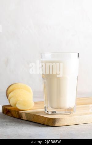 Vegetarische vegane Kartoffelmilch im Glas, Kartoffel gereinigte Knolle auf hölzernen Küchenbrettern auf neutralem Hintergrund. Gesundes Getränk. Ersatz für nicht milchfreie Milch. Auswahl Stockfoto