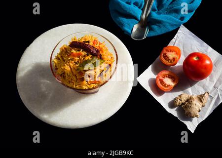 Würziger Tomatenreis oder Tamatar Pilaf oder Pulav, ist südindisches vegetarisches Gericht mit den Laub-Laub, Chilis.Glass Schüssel auf schwarzem Hintergrund.Draufsicht, Nahaufnahme. Stockfoto