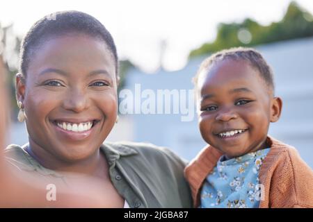 Lächeln Sie für das Selfie. Ein entzückendes kleines Mädchen, das mit ihrer Mutter in einem Garten Selfies macht. Stockfoto