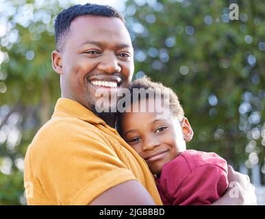 Mein kleiner Kerl, der Apfel meines Auges. Ein entzückender kleiner Junge umarmt seinen Vater in einem Garten. Stockfoto