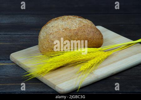Brot mit gelben Dornen auf Holzbrett. Dunkelgrauer Hintergrund Stockfoto