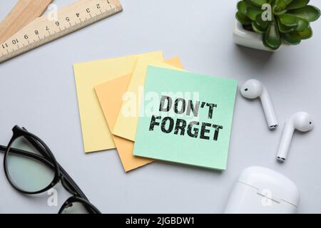 Haftnotiz mit Text NICHT VERGESSEN, Brille, Kopfhörer und Lineal auf hellem Hintergrund Stockfoto