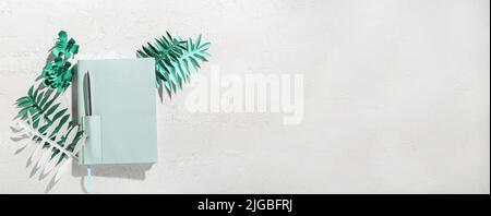 Stilvolles Notizbuch mit Papier, Palmblättern und Blumen auf hellem Hintergrund mit Platz für Text Stockfoto