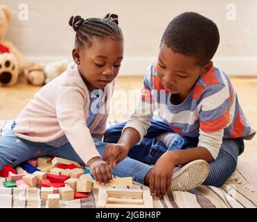 Sie bauen den höchsten Turm. Zwei Geschwister spielen zu Hause in ihrem Zimmer. Stockfoto