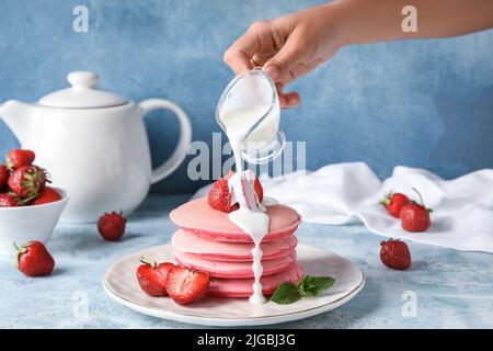 Frau gießt Sauce auf leckere rosa Pfannkuchen auf farbigen Hintergrund Stockfoto