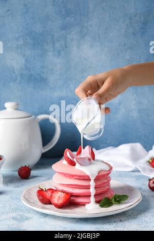 Frau gießt Sauce auf leckere rosa Pfannkuchen auf farbigen Hintergrund Stockfoto