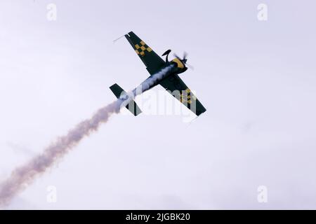 Gera, Deutschland. 09.. Juli 2022. Ein Pilot führt bei den Deutschen Aerobatic-Meisterschaften 300 Kunstflugfiguren mit einer Kunstflugmaschine Extra in der Luft durch und sprüht weißen künstlichen Nebel. Nach Angaben des Veranstalters nahmen 30 Teilnehmer aus Deutschland und Luxemburg an der Meisterschaft Teil. Kredit: Bodo Schackow/dpa/Alamy Live Nachrichten Stockfoto