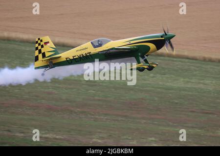 Gera, Deutschland. 09.. Juli 2022. Ein Pilot hebt mit einer Kunstflugmaschine Extra 300 bei den Deutschen Aerobatic Championships ab und sprüht dabei weißen künstlichen Nebel. Nach Angaben des Veranstalters nahmen 30 Teilnehmer aus Deutschland und Luxemburg an der Meisterschaft Teil. Kredit: Bodo Schackow/dpa/Alamy Live Nachrichten Stockfoto