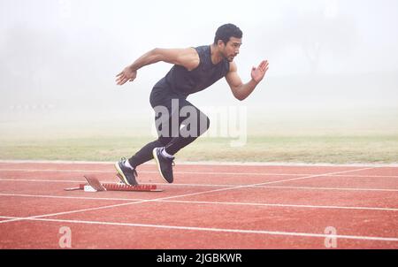 Das Rennen ist an. Ganzkörperaufnahme eines hübschen jungen Athleten, der auf einer Outdoor-Strecke läuft. Stockfoto