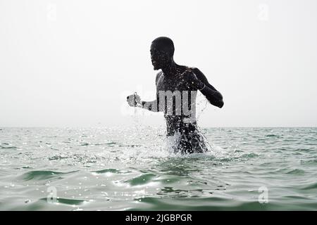Junger schwarzer Fußballspieler, der am frühen Morgen in Barcelona Aqua-Workout im Meer macht Stockfoto