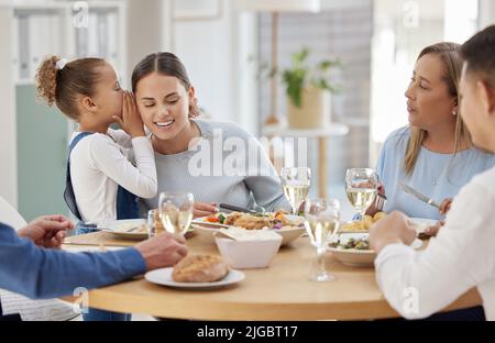 Ich brauche Hilfe im Töpfchen. Ein kleines Mädchen flüstert ein Geheimnis in das Ohr ihrer Mutter, während es zu Hause mit ihrer Familie zu Mittag gegessen hat. Stockfoto