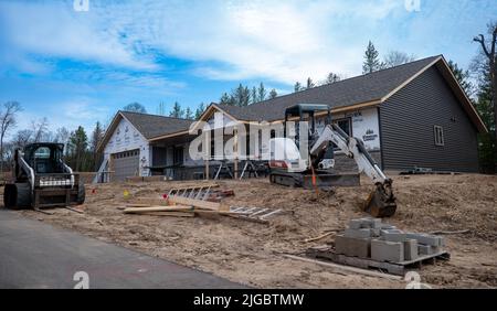 KRÄHENFLÜGEL CO, MN - 5. MAI 2022: Bobcat Minibagger und Frontlader, mit Gleitlenkerspuren, sitzen auf Schmutz vor einer neuen Wohnanlage. Stockfoto