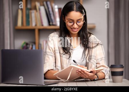 Shes bereit für das Finale. Eine attraktive junge Studentin, die sich Notizen macht, während sie mit ihrem Laptop in der Bibliothek studiert. Stockfoto