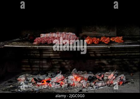Schweineribs und marinierte Hähnchenspieße, die auf einem Grillrost über Holzkohle kochen Stockfoto