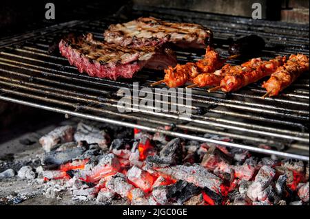 Schweineribs und marinierte Hähnchenspieße, die auf einem Grillrost über Holzkohle kochen Stockfoto