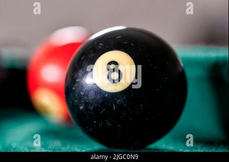 Schwarzer Billardball mit der Nummer 8 auf einem grünen Billardtisch mit anderen Bällen in der Nähe. Stockfoto