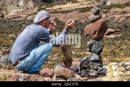 Dunbar, East Lothian, Schottland, Großbritannien, 9.. Juli 2022. European Stone Stacking Championship: Die Teilnehmer haben 3,5 Stunden Zeit, ein künstlerisches Kunstwerk aus den Felsen am Eye Cave Beach zu kreieren. Im Bild: Charlie Jordan, Steinstapler Stockfoto