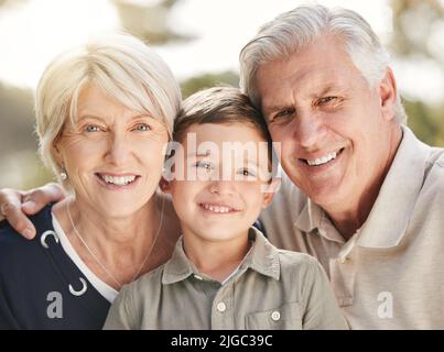 Portrait von liebenden kaukasischen Großeltern, die Zeit mit Enkel in der Natur genießen. Lächelnder kleiner Junge, der sich mit Großmutter und Großvater verbunden hat. Glücklich Stockfoto