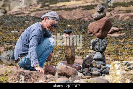 Dunbar, East Lothian, Schottland, Großbritannien, 9.. Juli 2022. European Stone Stacking Championship: Die Teilnehmer haben 3,5 Stunden Zeit, ein künstlerisches Kunstwerk aus den Felsen am Eye Cave Beach zu kreieren. Im Bild: Charlie Jordan, Steinstapler Stockfoto