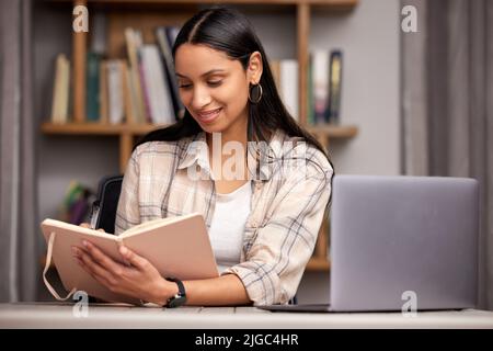 Das Finale wird ein Kinderspiel. Eine attraktive junge Studentin, die sich Notizen macht, während sie mit ihrem Laptop in der Bibliothek studiert. Stockfoto