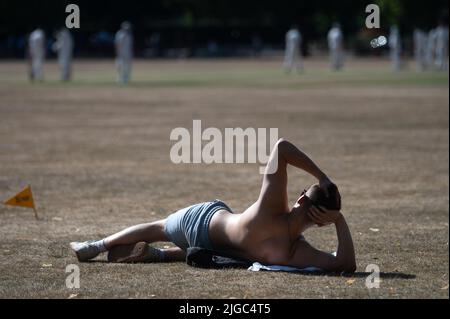 London, Großbritannien. 09.. Juli 2022. Ein Mann liegt auf einem ausgetrocknten Rasen, während Menschen im Hintergrund Cricket spielen. Quelle: Sebastian Gollnow/dpa/Alamy Live News Stockfoto