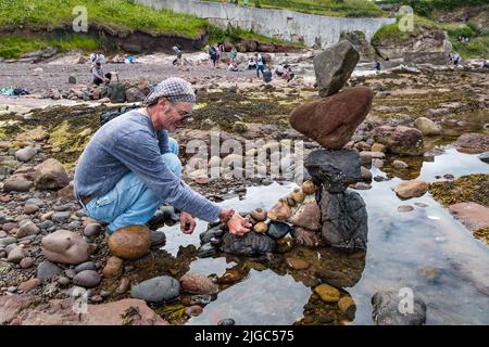 Dunbar, East Lothian, Schottland, Großbritannien, 9.. Juli 2022. European Stone Stacking Championship: Die Teilnehmer haben 3,5 Stunden Zeit, ein künstlerisches Kunstwerk aus den Felsen am Eye Cave Beach zu kreieren. Im Bild: Charlie Jordan, Steinstapler Stockfoto