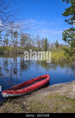 Rotes aufblasbares Kajak in der Nähe des Waldflusses. Frühlingswanderung zum Nationalpark. Stockfoto