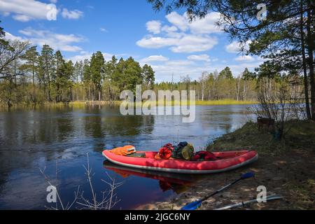 Rotes aufblasbares Kajak in der Nähe des Waldflusses. Frühlingswanderung zum Nationalpark. Stockfoto