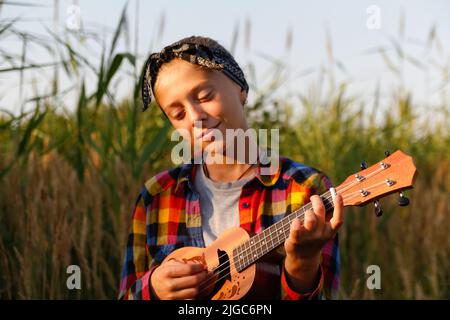 Defokussieren Mädchen mit Gitarre. Teen Mädchen zu Fuß auf Natur Hintergrund. Kleines Mädchen draußen auf grüner Wiese. Ukulelakkord. Sommerzeit. Menschen, Musiker. Stockfoto