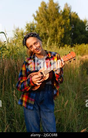 Defokussieren Mädchen mit Gitarre. Teen Mädchen zu Fuß auf Natur Hintergrund. Kleines Mädchen draußen auf grüner Wiese. Generation z. Herbst. Menschen und Musik. Dre Stockfoto